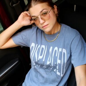 Casual portrait of a woman wearing sunglasses and a t-shirt sitting in a vehicle.