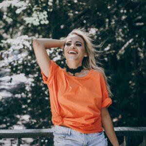 Cheerful woman enjoying the sunny weather in a vibrant orange shirt, embracing nature.