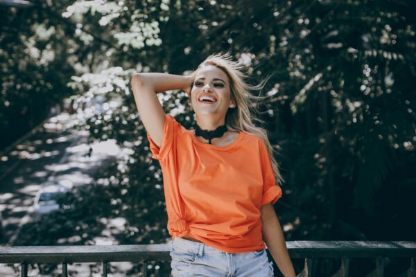 Cheerful woman enjoying the sunny weather in a vibrant orange shirt, embracing nature.