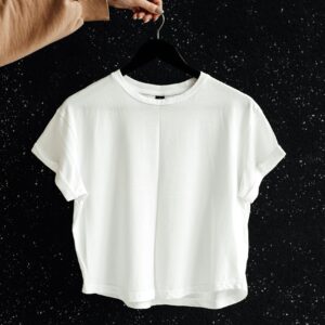White t-shirt on hanger against a speckled black wall, showcasing minimalist fashion.