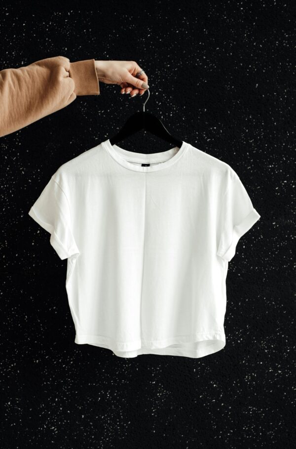 White t-shirt on hanger against a speckled black wall, showcasing minimalist fashion.