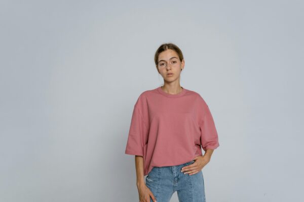 Portrait of a young woman standing in a relaxed pose wearing a pink t-shirt and jeans.