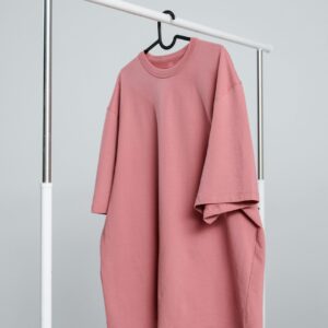 A minimalist pink unisex t-shirt hanging on a white rack against a light background.